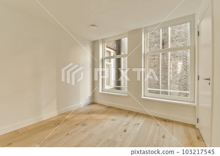 an empty room with white walls and wood flooring, there is a large window in the wall has a brick pattern on it 103217545