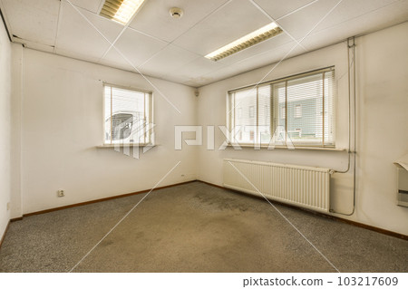 an empty room with white walls and grey carpet on the floor, there is a window that has blinds in it 103217609