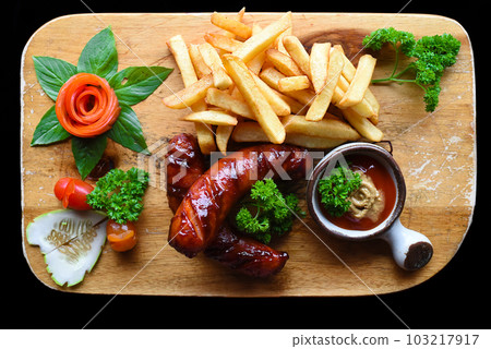 Fried sausages with french fries and spicy sauce on wooden board isolated on black background top view 103217917