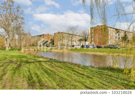 some buildings and water in the middle of an urban area with green grass, trees and blue sky above it 103218026