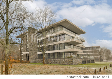 a very modern house in the middle of an urban area with trees and grass on the ground is covered with dead leaves 103218461
