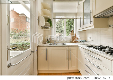 a kitchen with wood flooring and white cabinetd cupboards on either side of the window looking out onto the street 103218793