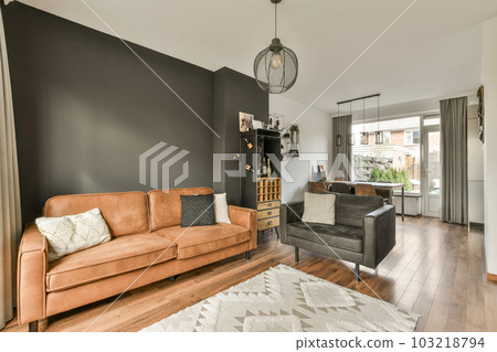 a living room with black walls and hardwood flooring, including a brown leather couch in the center of the room 103218794