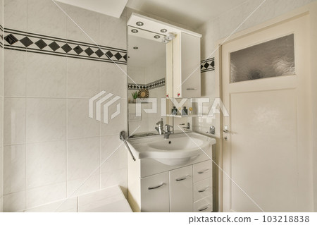 a white bathroom with black and white tiles on the wall behind it is a sink, mirror and toiletries a white bathroom with black and white tiles on the wall behind it is a sink, mirror and toiletries 103218838