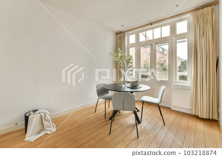 a living room with wood flooring and white walls, there is a small round dining table in front of the window 103218874