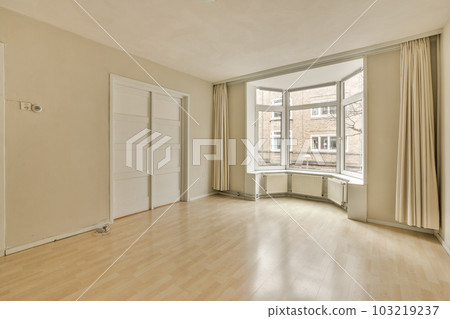 an empty living room with wood flooring and large windows looking out onto the street in front of the house an empty living room with wood flooring and large windows looking out onto the street in front of the house 103219237