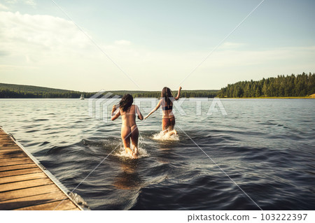 Two young women splashing in the water on a wooden pier. Generative AI 103222397