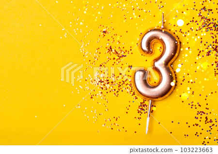 Gold candle in the form of number three on yellow background with confetti. 103223663