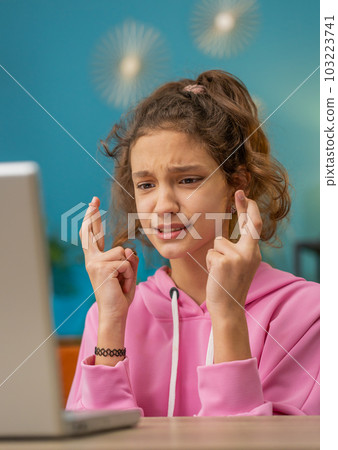 School girl looking at laptop screen crossed fingers wishing good exam results dreaming about win 103223741