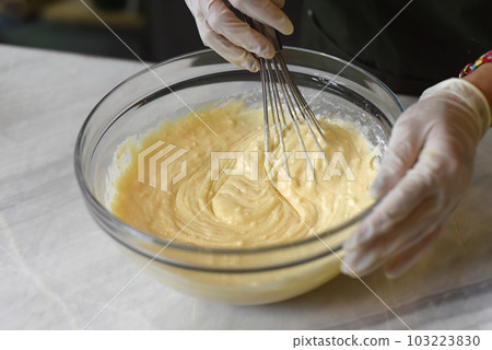 A hand in rubber glove stirring  dough for a cake   103223830
