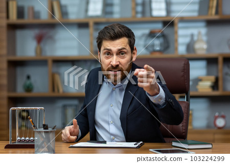 Portrait of an angry young businessman talking on a video call in the office with clients, team, partners. Unsatisfied with work, burning deadlines, firing from a job. 103224299
