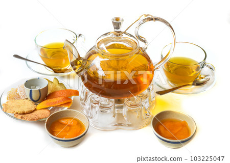 Glass tea pot with plum mango tea and ham,cups and crystalized fruits on white background Glass tea pot with plum mango tea and ham,cups and crystalized fruits on white background 103225047