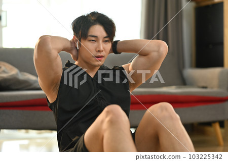 Fit muscular asian man doing abdominal sit ups in living room. Fitness, training and healthy lifestyle concept Fit muscular asian man doing abdominal sit ups in living room. Fitness, training and healthy lifestyle concept 103225342