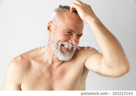 Portrait of handsome, mature, half-naked man with gray hair and beard smiling against grey background. Morning routine 103227243