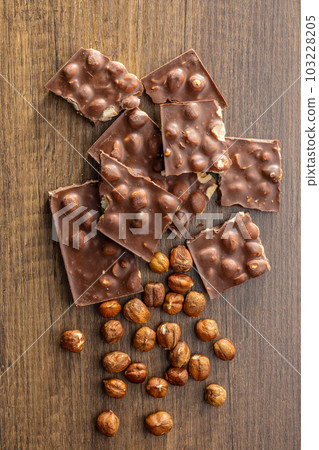 Broken chocolate bars with nuts on wooden table.. Top view. Broken chocolate bars with nuts on wooden table.. Top view. 103228205
