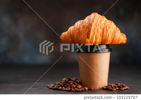 Aromatic coffee in a paper cup paired with a flaky croissant Aromatic coffee in a paper cup paired with a flaky croissant 103229787