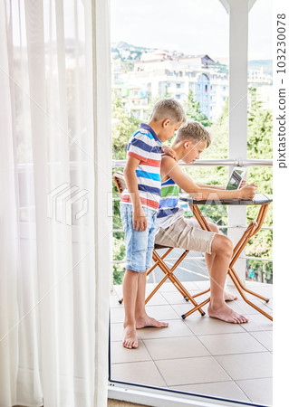 Junior schoolboy watches preteen brother playing difficult games on laptop. Boys siblings spend together summer holidays at seaside resort Junior schoolboy watches preteen brother playing difficult games on laptop. Boys siblings spend together summer holidays at seaside resort 103230078