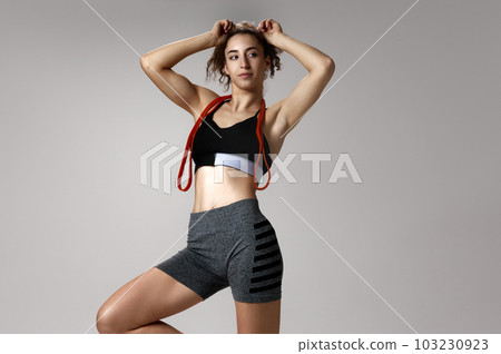 Portrait of young girl in sportswear with slim, fit body posing with fitness expanders against gray studio background 103230923