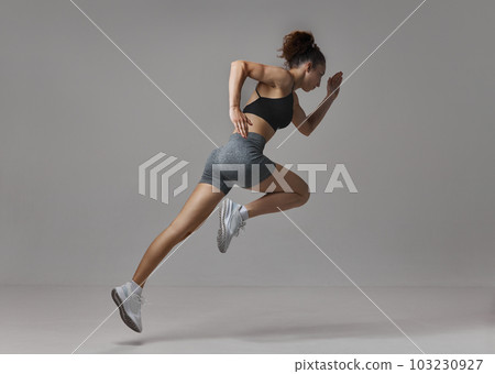 Dynamic image of sportive, young, strong woman in sportswear training, running against gray studio background Dynamic image of sportive, young, strong woman in sportswear training, running against gray studio background 103230927