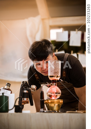 Professional coffee maker - Barista using coffee siphon brewing hot espresso at coffee shop coffee brewing syphon alternative method. Startup Business Concept. Professional coffee maker - Barista using coffee siphon brewing hot espresso at coffee shop coffee brewing syphon alternative method. Startup Business Concept. 103233263