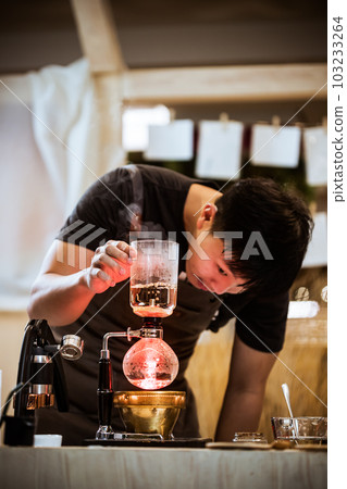 Professional coffee maker - Barista using coffee siphon brewing hot espresso at coffee shop coffee brewing syphon alternative method. Startup Business Concept. Professional coffee maker - Barista using coffee siphon brewing hot espresso at coffee shop coffee brewing syphon alternative method. Startup Business Concept. 103233264