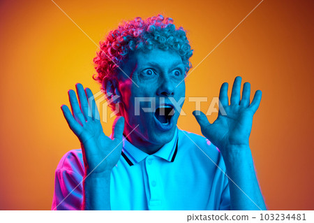 Shock. Portrait of mature man with curly hair spreading hands in surprise against orange studio background in blue neon light Shock. Portrait of mature man with curly hair spreading hands in surprise against orange studio background in blue neon light 103234481