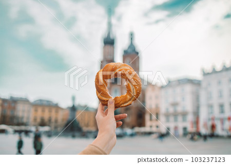 Tourist woman hand holding bagel obwarzanek, traditional polish snack in old city center view in Krakow, Europe. Back view Tourist woman hand holding bagel obwarzanek, traditional polish snack in old city center view in Krakow, Europe. Back view 103237123