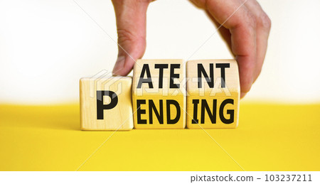 Patent pending symbol. Concept words Patent pending on wooden cubes. Businessman hand. Beautiful yellow table white background. Business and patent pending concept. Copy space. 103237211