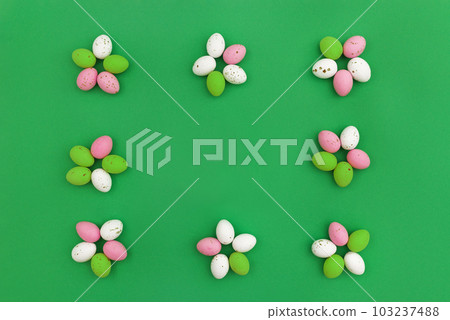 Happy Easter concept. Colorful chocolate eggs arranged in shape of flowers, which form frame on green background. Use for Easter or spring advertising as decorative image for blog. Top view.Copy Space 103237488