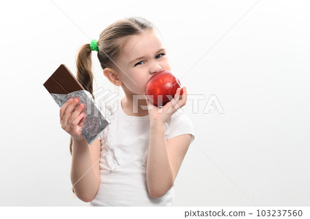 Little cute girl chooses apple over chocolate, preference of healthy food over unhealthy and unhealthy. Little cute girl chooses apple over chocolate, preference of healthy food over unhealthy and unhealthy. 103237560