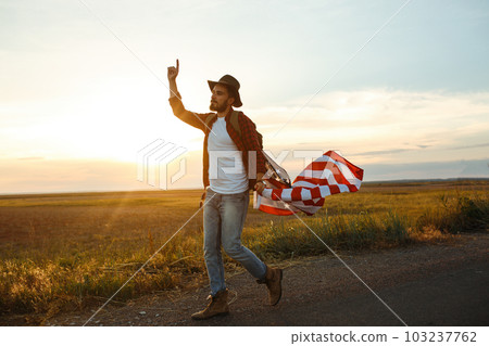 4th of July. American Flag. Traveler with the flag of America. The man in a hat, a backpack, a shirt and jeans. 103237762