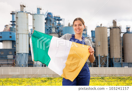 Happy young woman worker with flag of Ireland against background of factory Happy young woman worker with flag of Ireland against background of factory 103241157