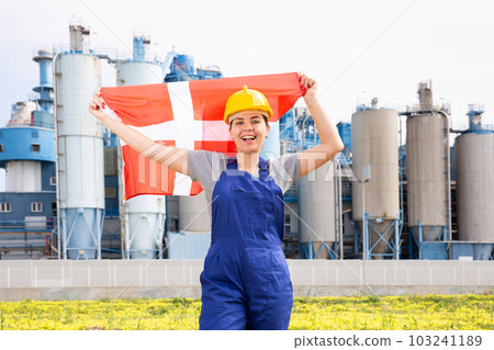 Happy girl in work clothes and hardhat with flag of denmark standing in front of industrial scenery Happy girl in work clothes and hardhat with flag of denmark standing in front of industrial scenery 103241189