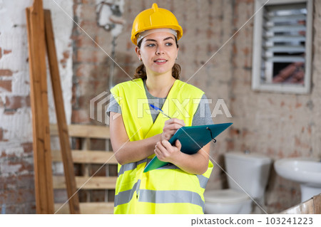 Smiling female civil engineer standing with papers at construction site Smiling female civil engineer standing with papers at construction site 103241223