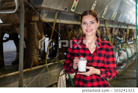 Female milker posing with glass of milk on dairy farm Female milker posing with glass of milk on dairy farm 103241321