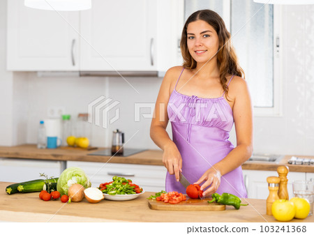 Smiling young housewife in purple nightgown cooking dinner in kitchen at home 103241368
