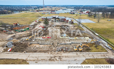 Outline of destroyed building and a ripped open half of another building with construction vehicles 103243863