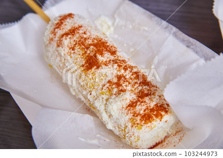 Elotes elote corn street food Mexican food dish cotija cheese spicy chili powder on white dish Elotes elote corn street food Mexican food dish cotija cheese spicy chili powder on white dish 103244973