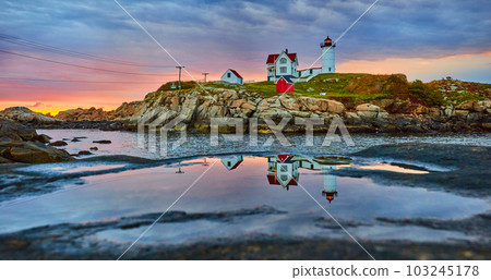 Maine lighthouse reflecting in puddle on rock during golden morning light with overcast clouds Maine lighthouse reflecting in puddle on rock during golden morning light with overcast clouds 103245178