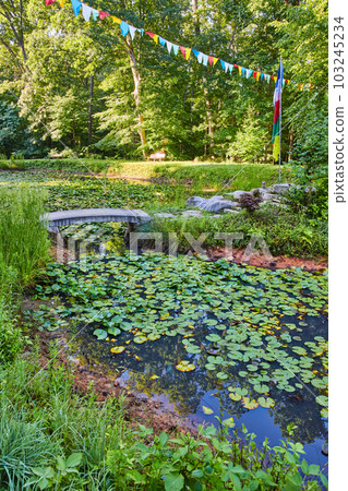 Lily pond in Tibetan Mongolian Buddhist temple with prayer flags and walking bridge to small island Lily pond in Tibetan Mongolian Buddhist temple with prayer flags and walking bridge to small island 103245234