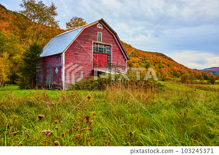 Red barn in country fields surrounded by mountains of peak fall foliage trees 103245371