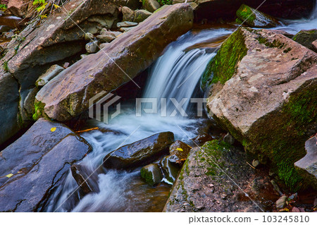 Up close to waterfall pouring over mossy boulders in detail 103245810