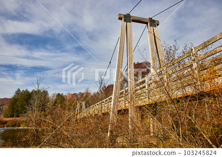 View below large suspension bridge going over river near fall fields and forests View below large suspension bridge going over river near fall fields and forests 103245824
