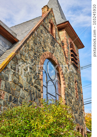 Looking up side of stone church in small town with glass window and simple steeple 103245910
