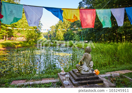 Lily pond from behind Tibetan Mongolian Buddhist statue with prayer flags overhead 103245911