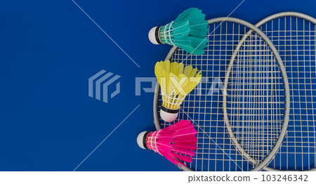 Colorful shuttlecocks and badminton rackets over blue Colorful shuttlecocks and badminton rackets over blue 103246342