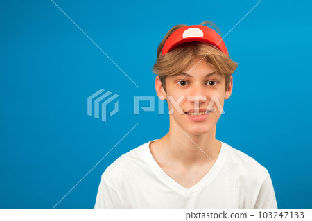 Let me think. Portrait of a cheerful handsome seller wearing a white t-shirt and a visor on his head in a studio on a blue background Let me think. Portrait of a cheerful handsome seller wearing a white t-shirt and a visor on his head in a studio on a blue background 103247133