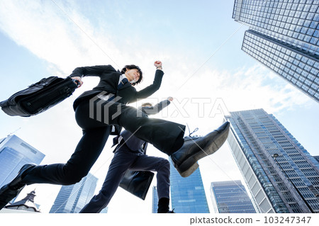 兩個西裝革履的商人在藍天高樓林立的城市中奔跑 兩個西裝革履的商人在藍天高樓林立的城市中奔跑 103247347