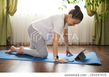 African American active pregnant woman using smartphone during online yoga practice, standing in table posture on a blue exercise mat. Pregnancy. Maternity. People. Sport. technology. Mobile app. 103247470