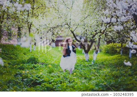Little girl in black jacket and white dress running in the spring cherry garden Little girl in black jacket and white dress running in the spring cherry garden 103248395